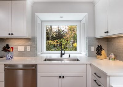 Modern kitchen with white cabinetry, stainless steel appliances, and a large window showcasing an autumn landscape, featuring a sink and knife block, highlighting home renovation aesthetics.