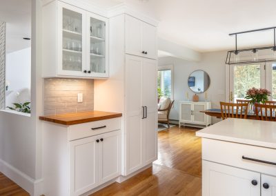Modern kitchen with white cabinetry, wooden countertop, and glass-front cabinet, showcasing a bright and inviting layout that emphasizes family gathering and functionality.